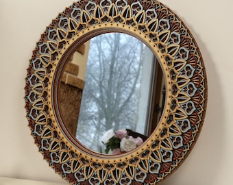 May include: A round, ornate mirror with a gold and brown frame featuring intricate geometric designs. The mirror reflects a view of trees and a cloudy sky.