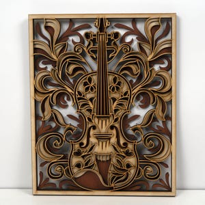 Puede incluir: Una obra de arte de madera en capas con un diseño de violín. La obra presenta un violín en el centro, rodeado de intrincados patrones florales y de volutas. La pieza está enmarcada en madera clara, con capas marrones oscuras y beige.