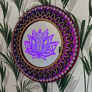 May include: A round wooden mirror with a decorative mandala design in shades of red, blue, and gold. The mirror reflects a purple lotus flower.