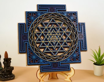 May include: A blue and gold wooden Sri Yantra mandala with intricate geometric patterns. The mandala is mounted on a wooden stand.