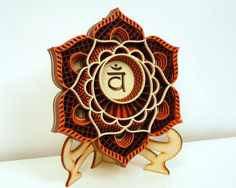 May include: A wooden mandala with a layered design in shades of orange and brown. The mandala features a central circle with the Sanskrit symbol "Svadhisthana" and a flower-like design.