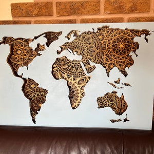 Puede incluir: Un mapa del mundo blanco con un dise&ntilde;o recortado. Los continentes est&aacute;n delineados en blanco y el fondo est&aacute; lleno de intrincados patrones de mandalas dorados.