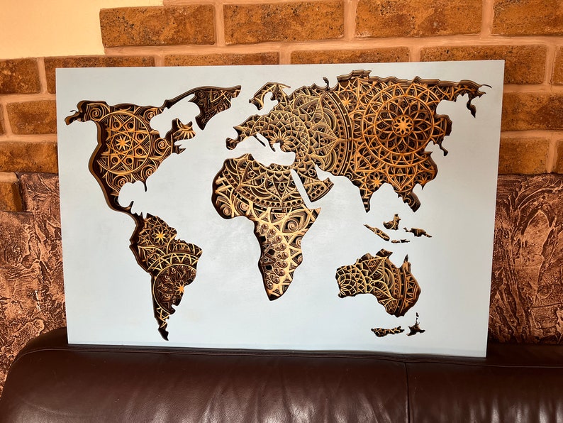 Puede incluir: Un mapa del mundo blanco con un dise&ntilde;o recortado. Los continentes est&aacute;n delineados en blanco y el fondo est&aacute; lleno de intrincados patrones de mandalas dorados.