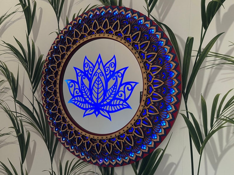May include: A round wooden mirror with a blue lotus flower design in the center. The mirror is surrounded by a decorative mandala pattern in shades of brown and blue.