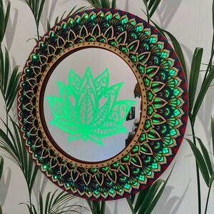 May include: A round mirror with a decorative wooden frame featuring a green lotus flower design. The frame is intricately carved with a mandala pattern in shades of red, blue, and gold.