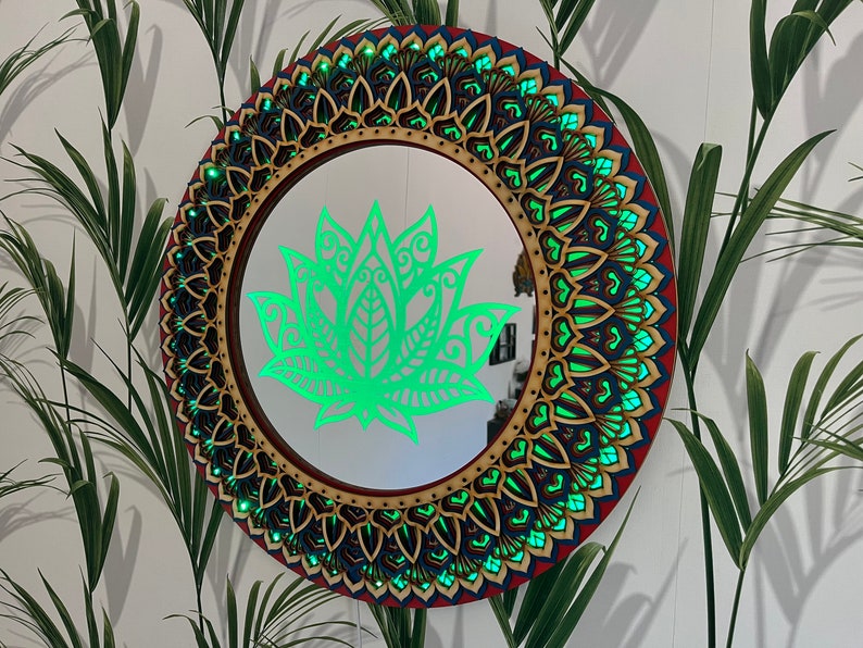 May include: A round mirror with a decorative wooden frame featuring a green lotus flower design. The frame is intricately carved with a mandala pattern in shades of red, blue, and gold.
