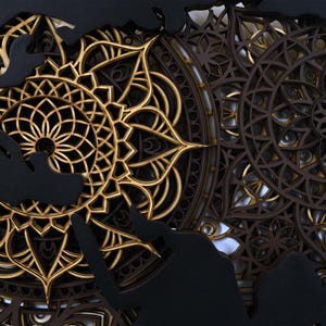 Puede incluir: Un dise&ntilde;o de mandala negro y dorado con detalles intrincados. El mandala est&aacute; hecho de madera y tiene un efecto de capas.