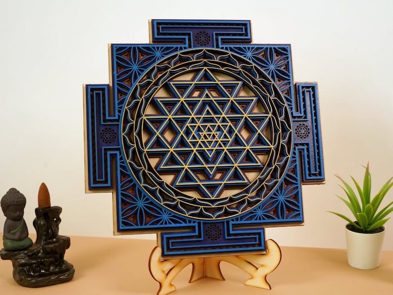 May include: A blue and gold Sri Yantra mandala with intricate geometric patterns, laser cut from wood and mounted on a wooden stand.