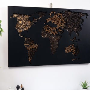 Puede incluir: Un mapa del mundo de madera negra con un dise&ntilde;o 3D que presenta intrincados patrones de mandala dorados. El mapa est&aacute; montado sobre un fondo negro.