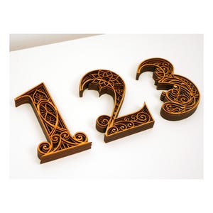 Op de afbeelding: Drie houten cijfers, 1, 2 en 3, zijn ingewikkeld gesneden met een decoratief bloemmotief. De cijfers zijn gelaagd en hebben een warme bruine kleur.