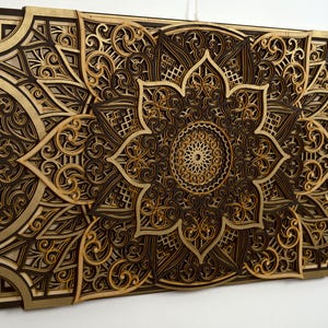 Intricate layered wooden mandala wall art with gold and dark brown tones displayed on a white wall.