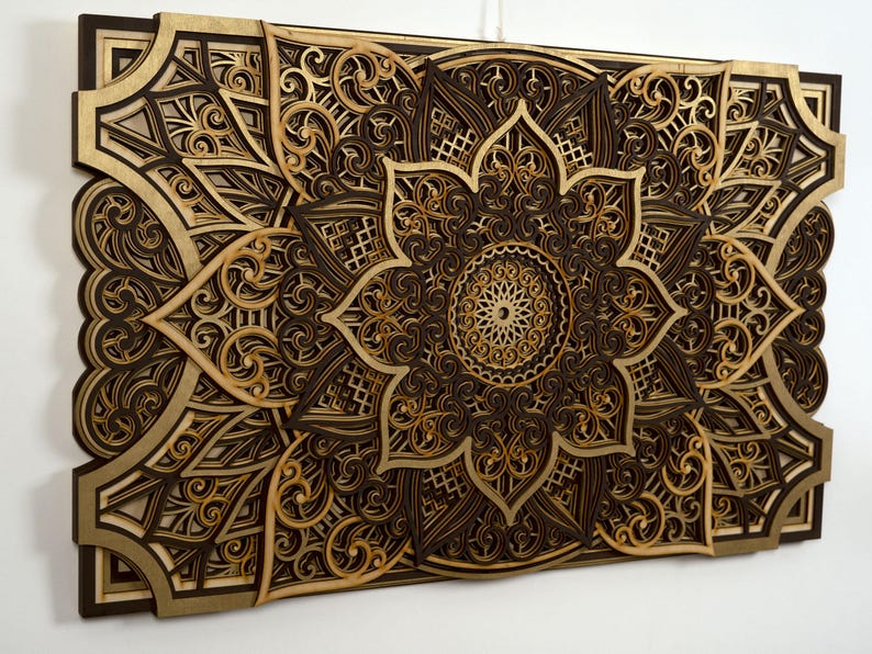 Intricate layered wooden mandala wall art with gold and dark brown tones displayed on a white wall.