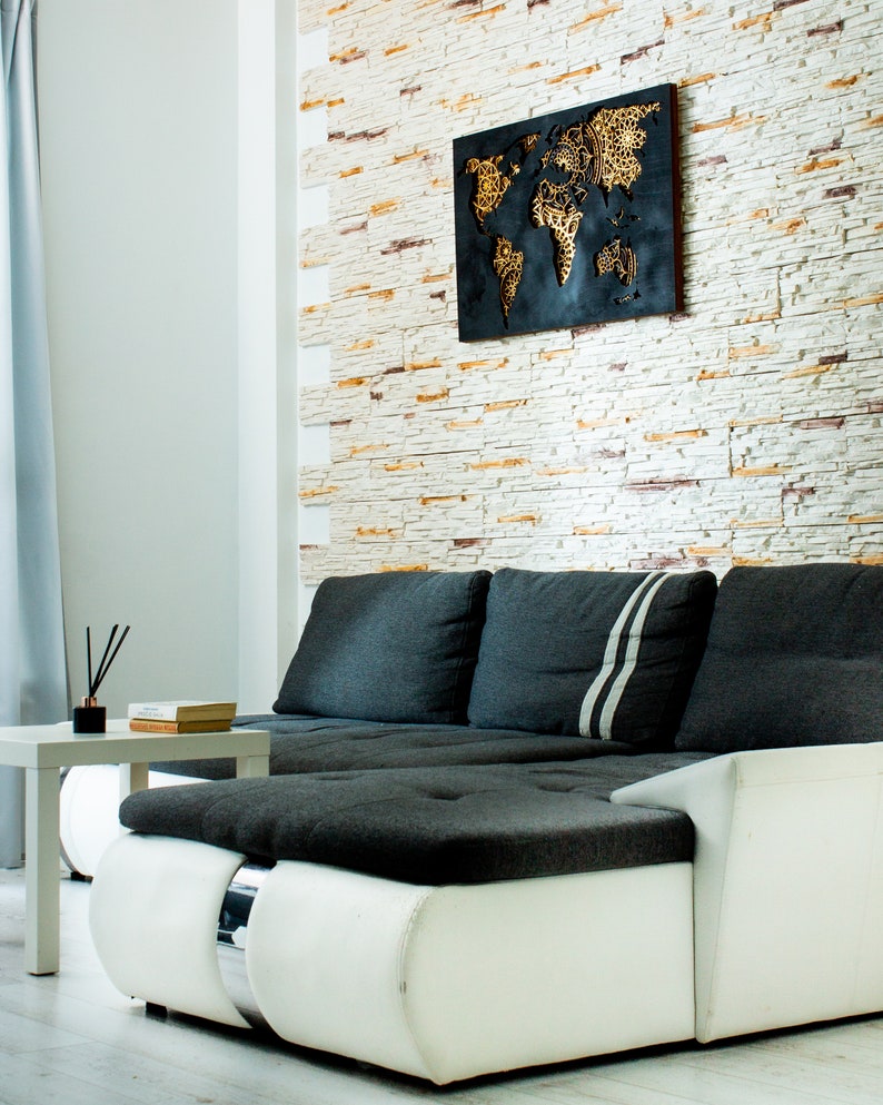 Puede incluir: Un sof&aacute; seccional blanco y gris con un coj&iacute;n de tela negro y una decoraci&oacute;n de pared de mapa del mundo negro y dorado en una pared de ladrillo blanco.