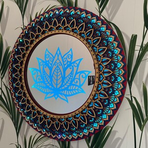 May include: A round wooden mirror with a blue and gold mandala design. The mirror has a blue lotus flower design in the center.