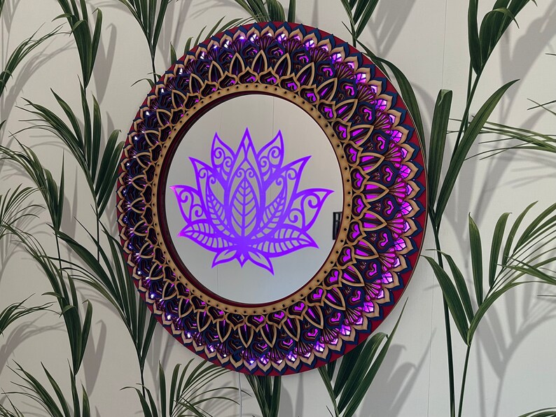 May include: A round wooden mirror with a decorative mandala design in shades of red, blue, and gold. The mirror reflects a purple lotus flower.