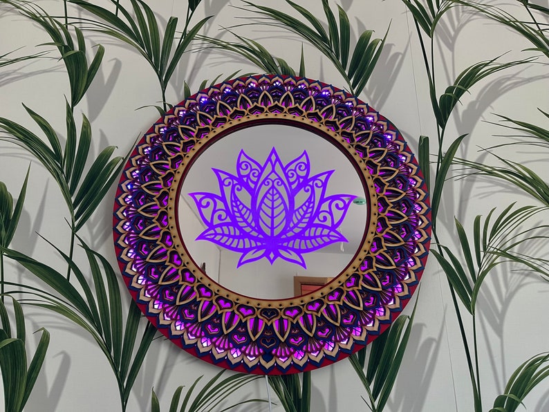 May include: A round wooden mirror with a purple mandala design and a purple lotus flower in the center. The mirror is surrounded by a decorative frame with a red and gold border.