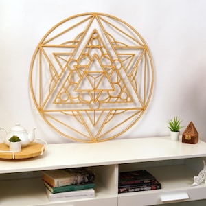 May include: A wooden geometric wall art piece in the shape of a star with a circular frame. The art is made of light brown wood and has an intricate design of overlapping triangles and circles.