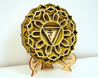 May include: A yellow and brown wooden mandala with a layered design. The mandala is on a wooden stand. The mandala features a symbol in the center.