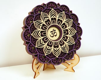 May include: A purple and cream layered mandala with the symbol "Om" in the center, mounted on a wooden stand.