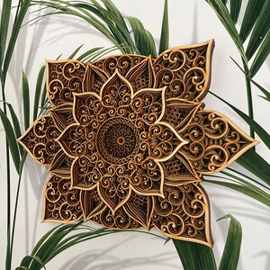 May include: A brown wooden mandala wall decor with intricate laser cut designs. The mandala features a flower-like pattern with a circular center.