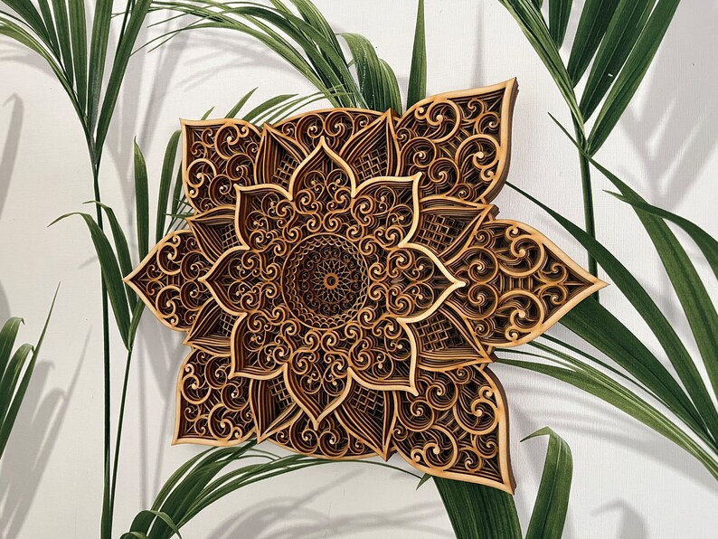 May include: A brown wooden mandala wall decor with intricate laser cut designs. The mandala features a flower-like pattern with a circular center.