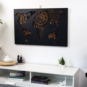 Puede incluir: Una decoraci&oacute;n de pared de mapa del mundo de madera negra con intrincados dise&ntilde;os de mandala recortados en color dorado.