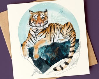 May include: A square greeting card featuring a detailed illustration of an orange and black tiger resting on a dark blue, textured rock formation. The tiger is set against a light blue circular background with faint fern leaf patterns.