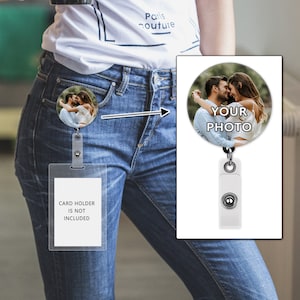 May include: A white retractable badge holder with a round photo insert featuring a couple. The photo insert says "YOUR PHOTO". The badge holder is attached to a pair of blue jeans.