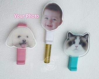 May include: Three personalized photo clips featuring a baby, a dog, and a cat. The clips have different colored bases: pink, white, and teal. The text "Your Photo" is visible in pink above the clips.