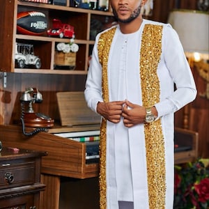 May include: White long-sleeved tunic and trousers with gold sequin detailing. The outfit has a mandarin collar and a button-down front. A gold wristwatch is also visible. The image includes the text "ZACK KEDDIES 0241811311".