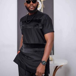 May include: A black outfit consisting of a short-sleeved shirt and trousers. The shirt has a velvet band across the chest and waist. The person is wearing sunglasses, a beaded necklace, and a wristwatch. The ensemble is a contemporary interpretation of classic clothing.