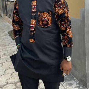 May include: Black traditional outfit with a lion design. The long-sleeved shirt features a lion-themed pocket and decorative accents. The outfit includes matching black trousers and a black cap. The sleeves have a floral pattern.