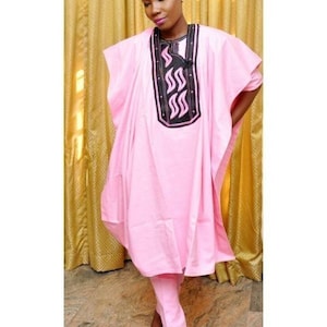 May include: A light pink, two-piece outfit with a tunic and trousers. The tunic has a black and white embroidered design on the neckline. The outfit is worn with black high heels with fur detailing.