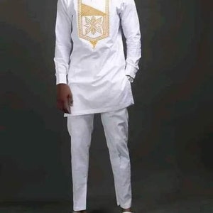 May include: A white tunic and trousers outfit with long sleeves. The tunic has a gold embroidered design on the chest. The outfit is completed with white slip-on shoes. This is a traditional style ensemble.