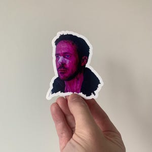 May include: A sticker depicting a man with a bandage on his nose and a black jacket, rendered in a pink and purple colour palette. The portrait is stylized, with the man's face and hair outlined in black.
