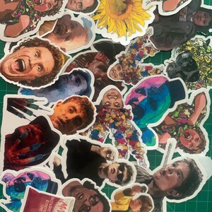 May include: A collection of colorful stickers featuring various characters and images, including a sunflower, a person with a red shirt, and a person with a blue shirt. The stickers are printed on white paper and have a glossy finish.
