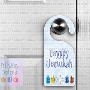 May include: A blue and white door hanger with the text "Happy Chanukah" and a design of five dreidels. The dreidels are decorated with the Hebrew letters "nun", "gimmel", "hey", and "shin".