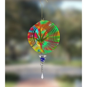 May include: A colorful, tie-dye wind spinner with a green marijuana leaf design. The spinner has a blue glass bead and a crystal-shaped hanging piece.