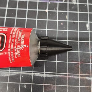 May include: A red tube of adhesive with a black nozzle. The tube has the word "WARNING" printed on it, along with the phrases "FLAMMABLE. IRRITANT." and "Read cautions carefully on back panel."
