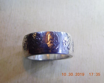 May include: A silver ring with a textured band and four raised designs. The designs are of a stylized heart, a cross, and two other abstract shapes.
