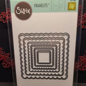 Puede incluir: Un paquete de seis marcos de metal troquelados para manualidades. El paquete es blanco con el logotipo de Sizzix y el texto "FRAMELITS" en azul. El paquete también incluye el texto "6 DIES | 6 MATRICES | 6 TROQUELES | 6 FUSTELLE | 6 ВЫРУБКИ | 6 STANZEN | 6 CORTANTES" en negro.