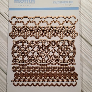 May include: A package of nine gold-colored metal die cuts for scrapbooking or card making. The package is labeled "Small Die of the Month" and "Styled Border Trio".