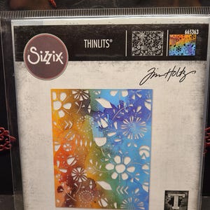 May include: A Sizzix Thinlits die featuring a rainbow floral design with a cut-out pattern. The die is labeled "665363" and "Jim Holtz". The packaging also includes the words "DIE | MATRICE | TROQUEL | FUSTELLA | ВЫРУБКА | STANZE | CORTANTE".