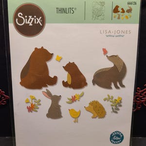 Puede incluir: Un conjunto de 11 formas troqueladas con animales del bosque, incluyendo osos, un tejón, un conejo, un erizo y un pájaro. Los troqueles están diseñados por Lisa Jones y forman parte de la colección Sizzix Thinlits. El paquete incluye el texto "666126", "LISA JONES" y "11 DIES | 11 MATRICES | 11 TROQUELES | 11 FUSTELLE | 11 ВЫРУБКИ | 11 STANZEN | 11 CORTANTES".