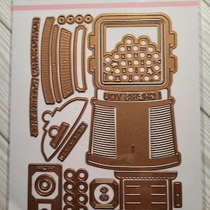 May include: A gold metal die set for a pop-up bubble gum machine. The set includes 26 dies and is part of the Spellbinders Clubs Die of the Month collection for September 2022. The dies are arranged on a white background with the text "DOMAPG-SEP22", "POP UP 3D VIGNETTE", "BUBBLE GUM MACHINE", and "26 Cutting Dies".