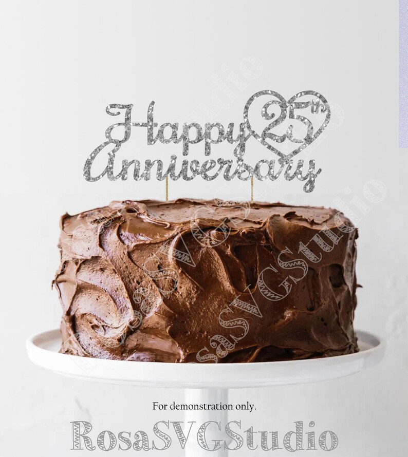 May include: Silver glitter cake topper with the text "Happy 25th Anniversary" and a heart with the number 25 inside. The topper is on top of a chocolate cake.