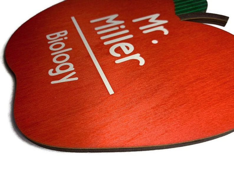 May include: Red apple-shaped wooden sign with white text that reads "Mr. Miller Biology".