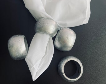 May include: Four silver napkin rings with a white linen napkin with an embroidered floral design.
