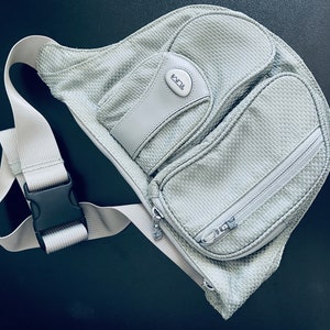 May include: A gray mesh sling bag with a zippered pocket and a black buckle strap. The bag has a white logo that says "ECCO" on the front.