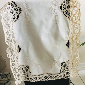 May include: White lace tablecloth with delicate embroidery. The lace trim features a scalloped edge and intricate floral patterns.